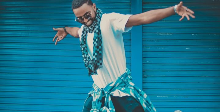 Dancing Male Artist Mann in modischer Kleidung mit Schal, vor einer blauen Wand posierend.